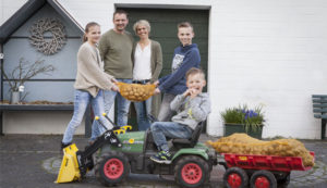 Bild: Familien hält Kartoffelsack, Kind davor auf Spielzeugtraktor mit Kartofelsack auf Anhänger